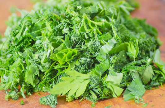 Pile of the chopped parsley and dill on the wooden cutting board closeup
