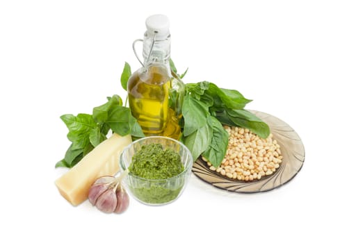 Sauce basil pesto in the small glass bowl and ingredients for its preparation on a white background
