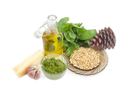 Sauce basil pesto in the small glass bowl on a background of ingredients for its preparation and pine cone on a white background
