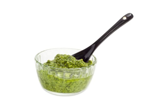 Sauce basil pesto in the small glass bowl with black ceramic small spoon on a white background
