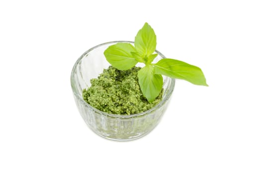 Sauce pesto in the small glass bowl decorated with green basil twig on a white background
