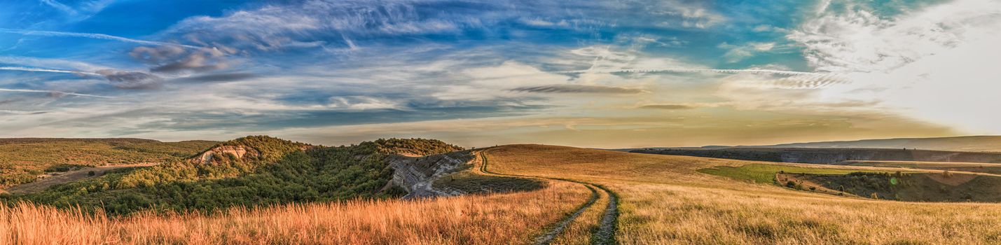 steppe road stretches into the distance to the rocks on the background of blue sky