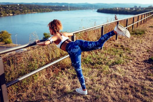 Young fitness woman with headphones doing exercise on the city rooftop.