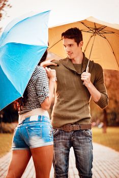 Beautiful lovely couple with umbrellas enjoying while walking in the rain through the park in autumn colors.