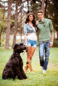 Beautiful lovely couple with a black giant schnauzer enjoying in the park.