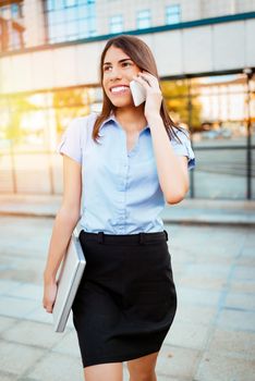 Young smiling businesswoman talking on smartphone in office district.