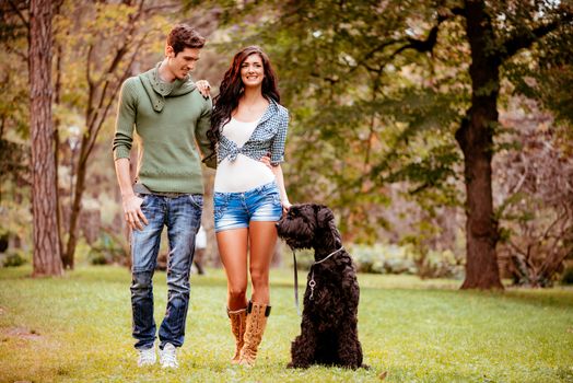 Beautiful lovely couple with a black giant schnauzer, enjoying and walking in the park.