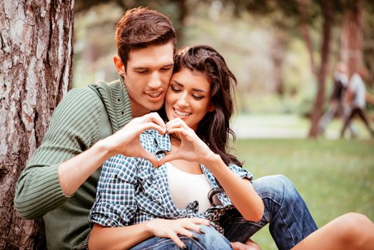 Beautiful lovely couple enjoying in park and with their hands making a heart shape.