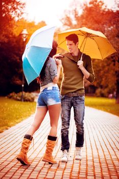 Beautiful lovely couple with umbrellas enjoying while walking in the rain through the park in autumn colors.