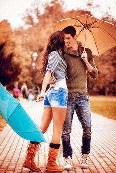 Beautiful lovely couple enjoying and dancing with umbrellas in the park in autumn colors.