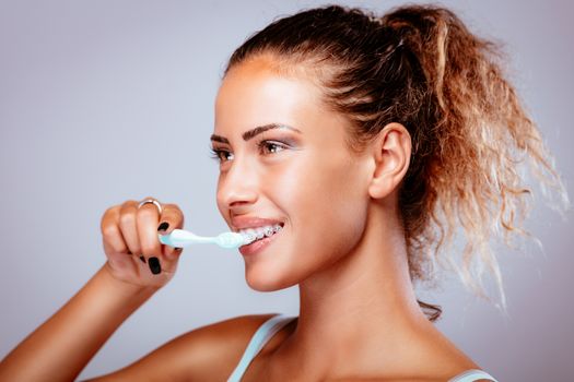 Smiling young woman with braces brushing her teeth.