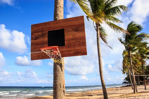 Basketball hoop on the beach with palm trees, sea, clouds and blue sky as a background