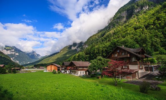 Beautiful panoramic postcard view of picturesque rural mountain scenery in the Alps with traditional old alpine mountain chalets and fresh green meadows on a sunny day with blue sky and clouds in the summer.