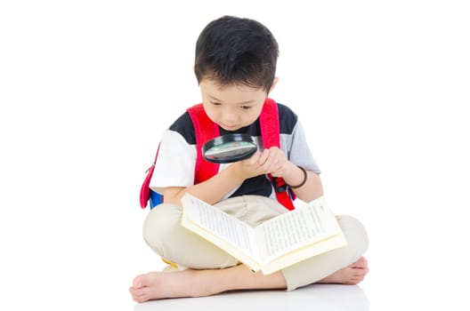 Asian preschool boy with schoolbag , magnifying glass and books sitting on the floor