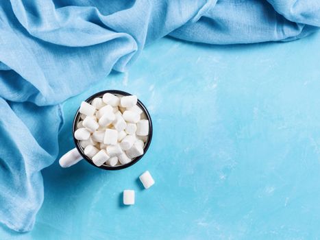 Marshmallows in cup on blue background with copyspace. Flat lay or top view. Background or texture of colorful mini marshmallows. Winter food background concept.