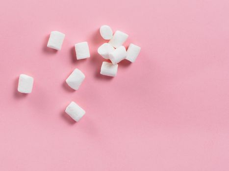 Marshmallows on pink background with copyspace. Flat lay or top view. Background or texture of colorful mini marshmallows. Winter food background concept.