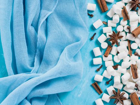 Marshmallows and winter spices on blue background with copyspace. Flat lay or top view. Background of colorful mini marshmallows, cinnamon, cloves and star anise. Winter food background concept.