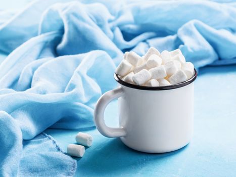 Marshmallows in cup on blue background with copyspace. Winter food background concept.