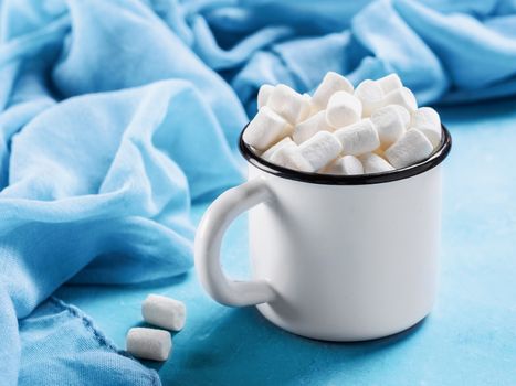 Marshmallows in cup on blue background with copyspace. Winter food background concept.