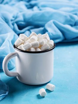 Marshmallows in cup on blue background with copyspace. Winter food background concept.