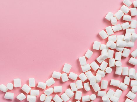 Marshmallows on pink background with copyspace. Flat lay or top view. Background or texture of colorful mini marshmallows. Winter food background concept.