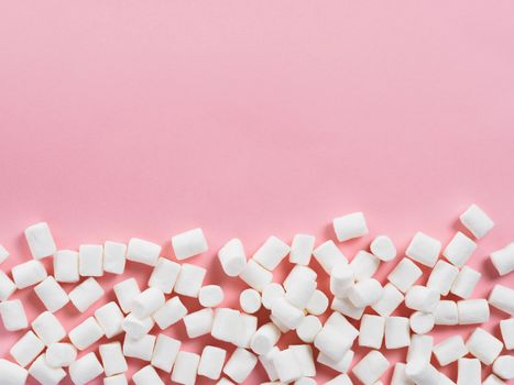 Marshmallows on pink background with copyspace. Flat lay or top view. Background or texture of colorful mini marshmallows. Winter food background concept.