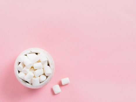 Marshmallows on pink background with copyspace. Flat lay or top view. Background or texture of colorful mini marshmallows. Winter food background concept.