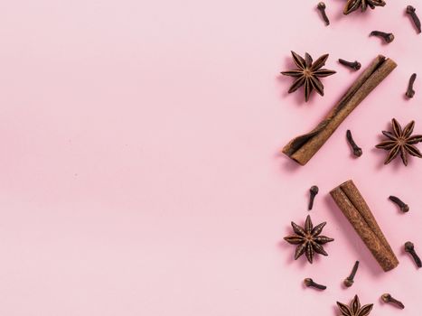 Winter spices on pink background with copyspace. Flat lay or top view. Background or texture of cinnamon, cloves and star anise. Winter food background concept.