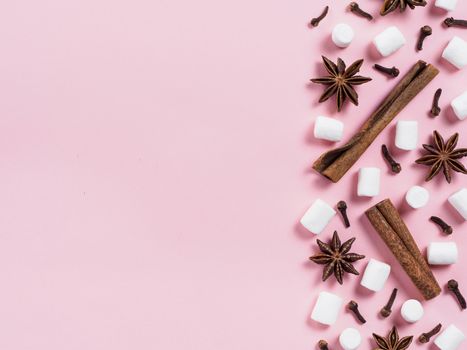 Marshmallows and winter spices on pink background with copyspace. Flat lay or top view. Background of colorful mini marshmallows, cinnamon, cloves and star anise. Winter food background concept.