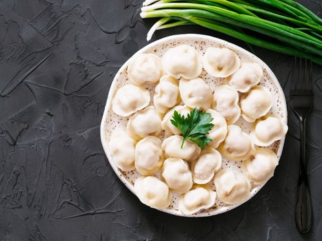Traditional russian pelmeni, ravioli, dumplings with meat on black concrete background. Copyspace. Top view or flat lay. Russian food and russian kitchen concept.