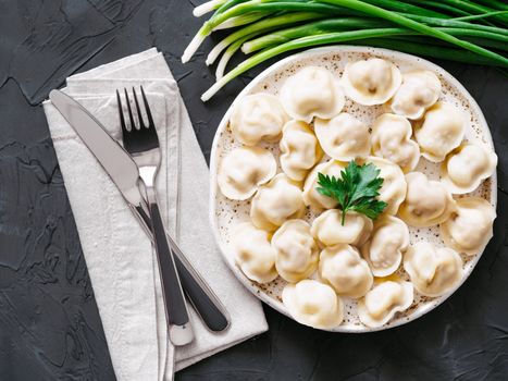 Traditional russian pelmeni, ravioli, dumplings with meat on black concrete background. Top view or flat lay. Russian food and russian kitchen concept.