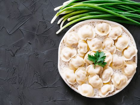 Traditional russian pelmeni, ravioli, dumplings with meat on black concrete background. Copyspace. Top view or flat lay. Russian food and russian kitchen concept.