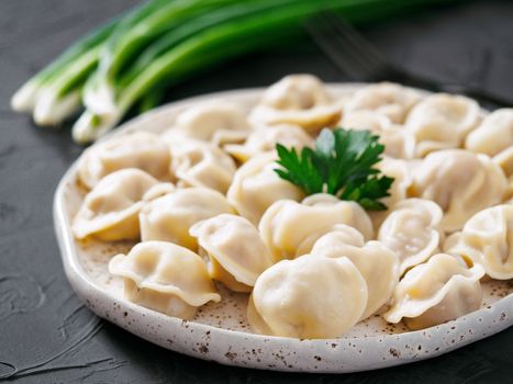 Traditional russian pelmeni, ravioli, dumplings with meat on black concrete background. Russian food and russian kitchen concept.