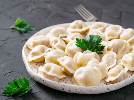 Traditional russian pelmeni, ravioli, dumplings with meat on black concrete background. Russian food and russian kitchen concept.