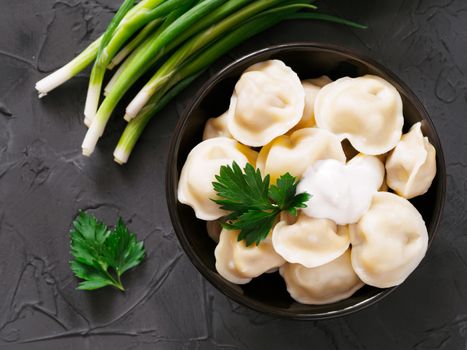 Traditional russian pelmeni, ravioli, dumplings with meat on black concrete background. Top view or flat lay. Russian food and russian kitchen concept.