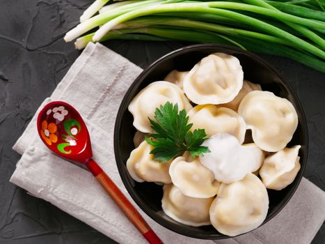Traditional russian pelmeni, ravioli, dumplings with meat on black concrete background. Top view or flat lay. Russian food and russian kitchen concept.