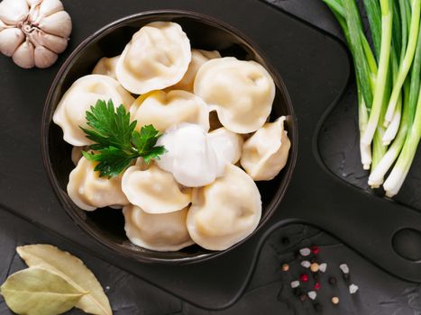 Traditional russian pelmeni, ravioli, dumplings with meat on black concrete background. Top view or flat lay. Russian food and russian kitchen concept.