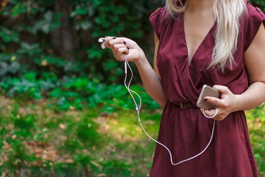 Headphones from a mobile phone in female hands. outdoors