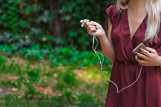 Headphones from a mobile phone in female hands. outdoors