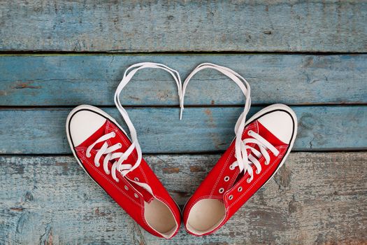 A pair of red retro sneakers on a blue wooden background, laces lined in a heart shape. Concept of young hipster love.