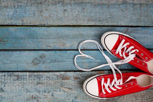 A pair of red retro sneakers on a blue wooden background, laces lined in a heart shape. Concept of young hipster love.