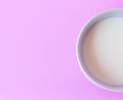 Closeup top view milk in white ceramic cup on pink background, selective focus