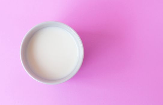 Closeup top view milk in white ceramic cup on pink background, selective focus
