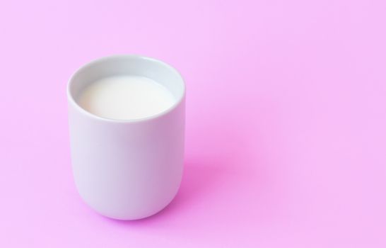 Milk in white ceramic cup on pink background, selective focus