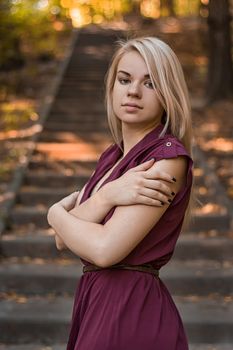 Portrait of young pretty white girl with blonde hair and in Burgundy clothes posing on the old stone staircase.
