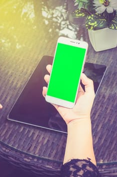 business woman working on Smartphone. There's a laptop nearby. Smartphone with green screen ready.