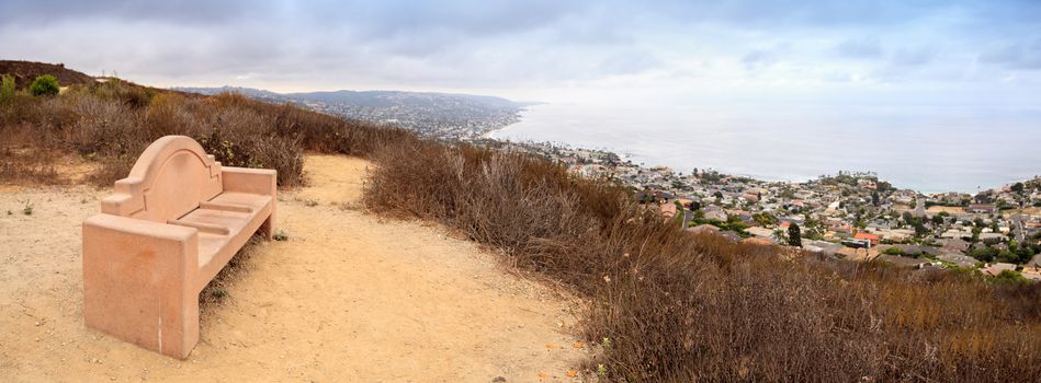 Dark rain clouds over a bench that overlooks the coastline of Laguna Beach, California, from the Laguna Coast Wilderness Park in summer.