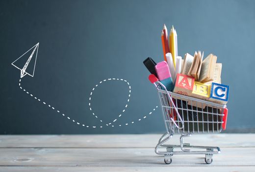 Shopping cart filled with stationery next to a chalkboard with a paper airplane sketch
