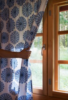 Hand opens curtain on the wooden cottage house window. Bright sunlight shines through. Beautiful summer morning light behind the window