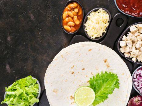 Traditional mexican tortilla with mix of ingredients on black concrete background with copy space